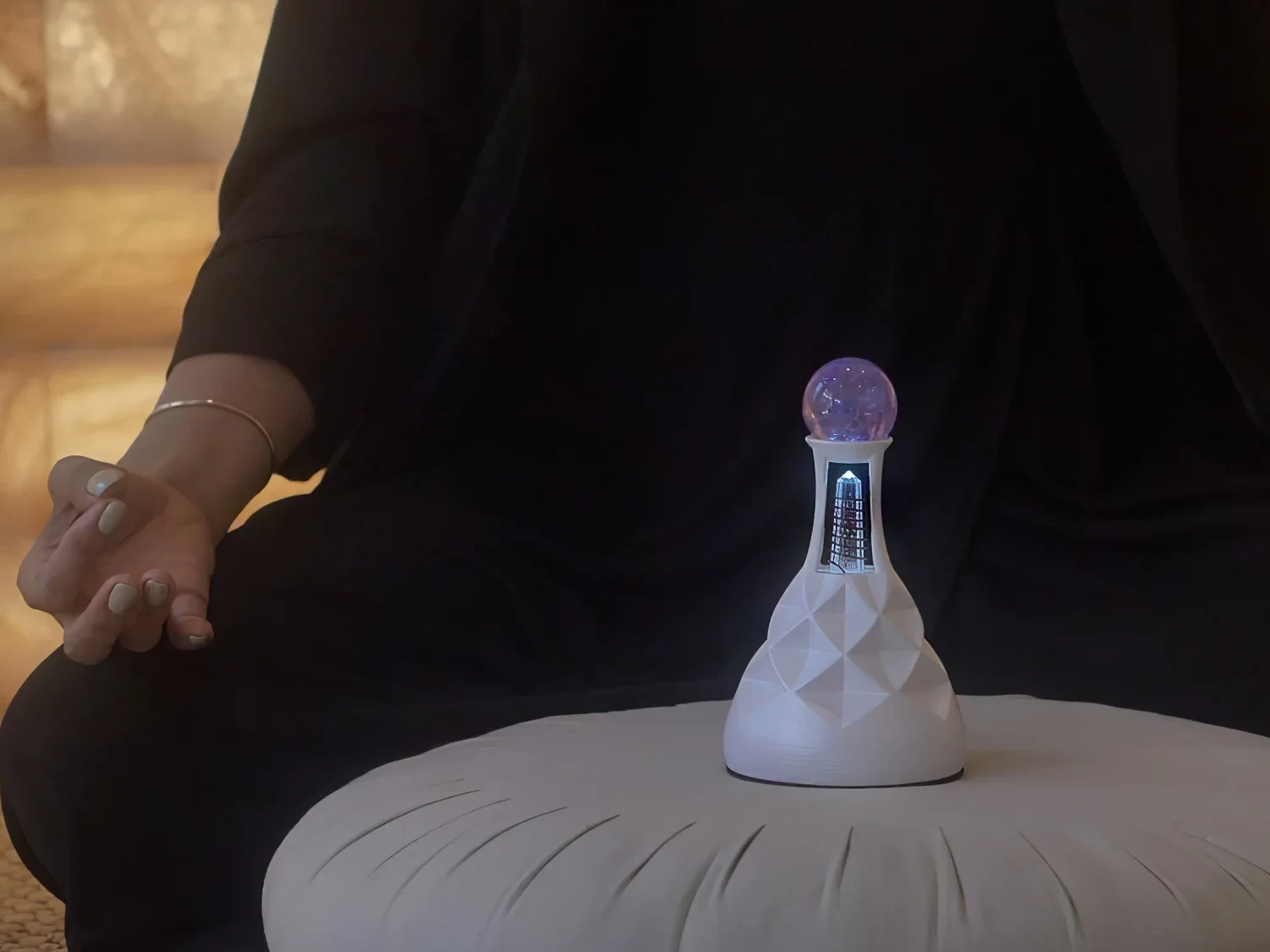 A practitioner seated in meditation with hands resting open, the Living Crystal glowing on the cushion before her
